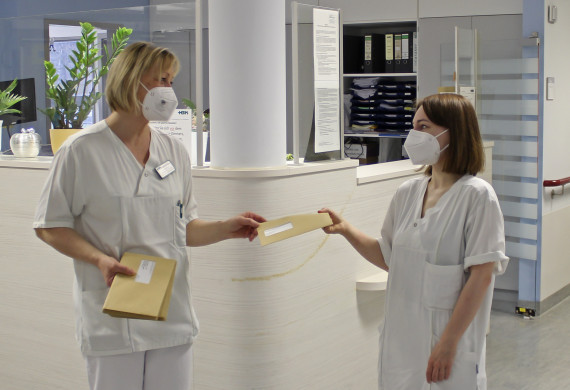 Jana Rohatzsch, Pflegerische Klinikleitung der Klinik für Neurorehabilitation (links), übergibt den Jubiläumsgruß an Gesundheits- und Krankenpflegerin Janine Nischwitz (rechts).